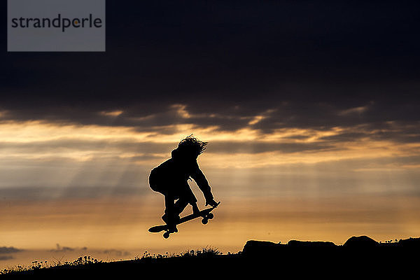 Junge Bursche beim Skateboarden bei Sonnenuntergang  beim Springen  in der Luft  Doolin  Clare  Irland