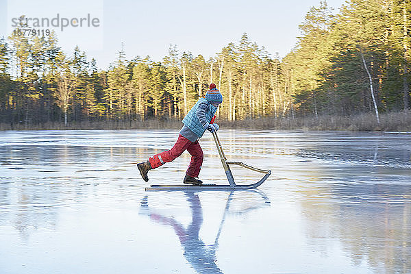 Junge fährt auf Schlitten über den gefrorenen See