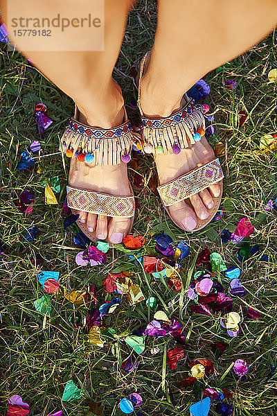 Draufsicht einer jungen Frau  die beim Holi-Fest zwischen Konfetti auf Gras steht  Detail der Füße