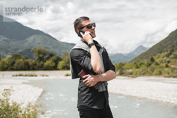 Geschäftsmann am Flussufer eines Gebirgsflusses telefoniert mit einem Smartphone  Francenigo  Venetien  Italien