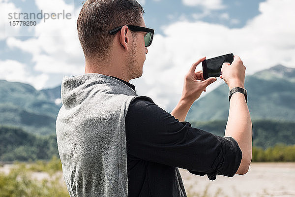 Männlicher Tourist beim Fotografieren eines Bergflusses mit einem Smartphone  Francenigo  Venetien  Italien