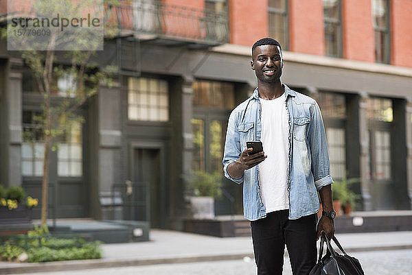 Junger Mann mit Handgepäck mit Handy in den Straßen von New York  USA
