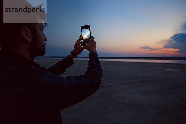 Mann mit Hut beim Fotografieren eines Sonnenuntergangs am Strand  Odessa  Ukraine