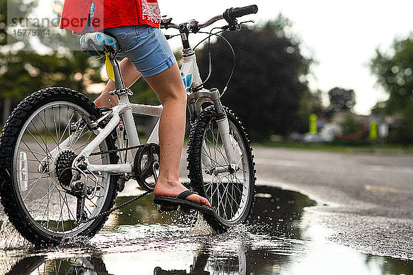 Mädchen fährt Fahrrad auf nasser Straße