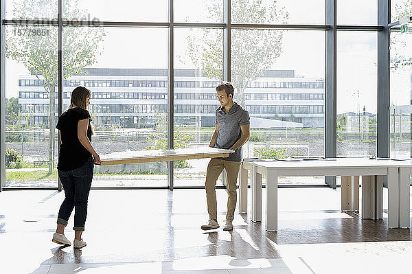 Zwei junge Architekten tragen ein maßstabsgetreues Gebäudemodell auf einen Tisch.