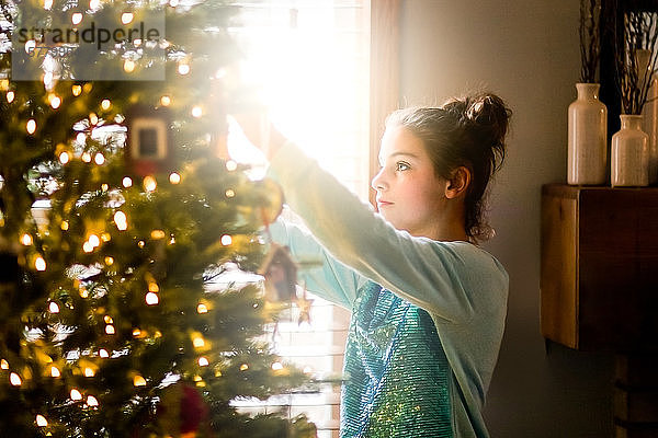 Junges Mädchen schmückt den Weihnachtsbaum zu Hause