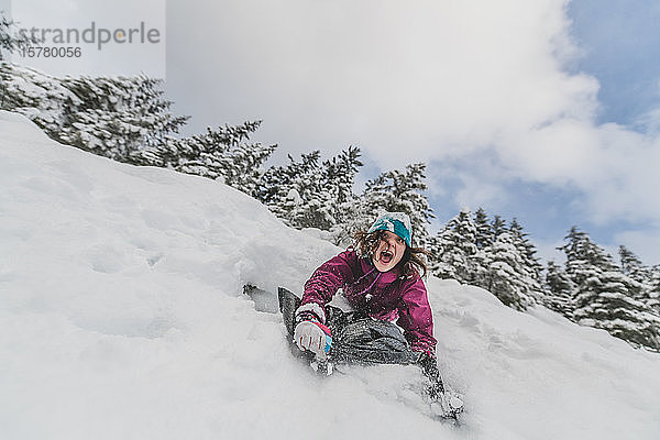 Frau  die in einem kanadischen Wald einen schneebedeckten Hang hinunterrutscht.