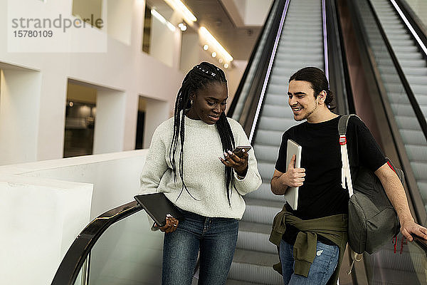 Zwei Studenten mit Handy auf einer Rolltreppe