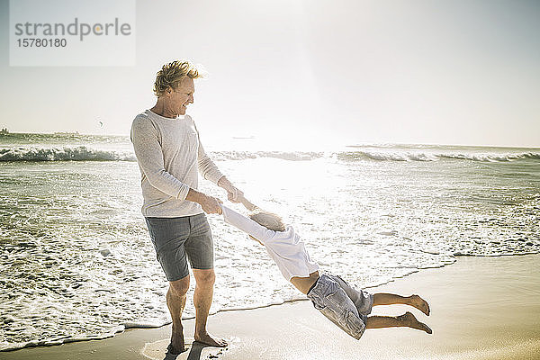 Vater amüsiert sich mit seinem Sohn am Strand und wirbelt ihn herum