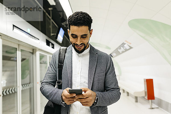 Junger Geschäftsmann benutzt Mobiltelefon in U-Bahn-Station