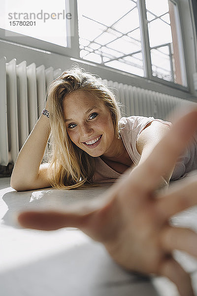 Porträt einer glücklichen blonden jungen Frau auf dem Boden liegend