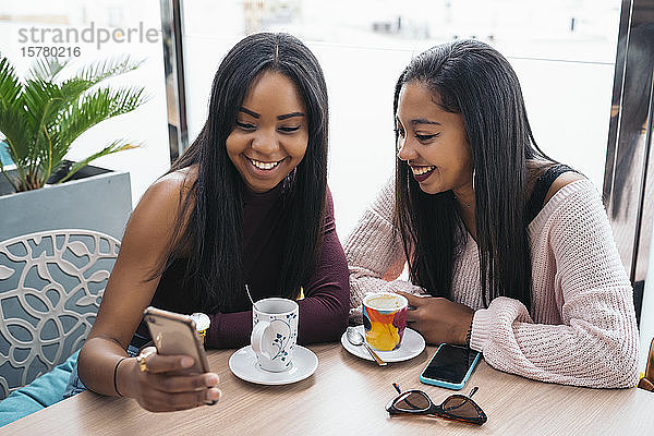 Zwei glückliche junge Frauen teilen sich ein Handy in einem Cafe