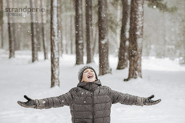 Porträt eines Jungen  der im Winterwald Schneeflocken fängt