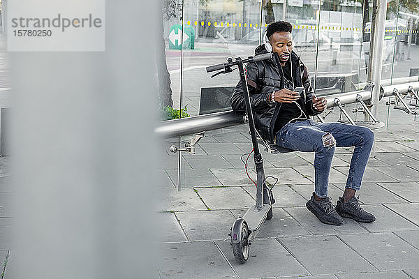 Mann mit Smartphone und E-Scooter an der Bushaltestelle