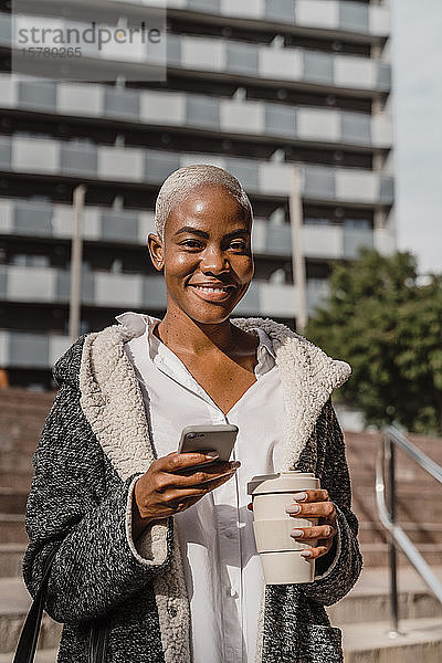 Stilvolle Geschäftsfrau  die mit Smartphone und Kaffeetasse durch die Stadt pendelt