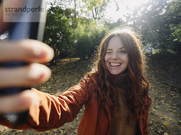 Glückliche rothaarige Frau  die im Herbst in einem Park ein Selfie macht