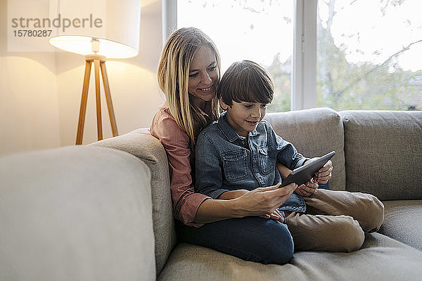 Mutter und Sohn sitzen auf dem Sofa und benutzen ein digitales Tablett