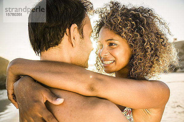 Glückliches Paar umarmt sich bei Sonnenuntergang am Strand