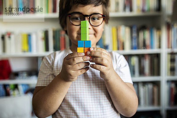 Lächelnder kleiner Junge mit Brille  der zu Hause mit Bauklötzen spielt