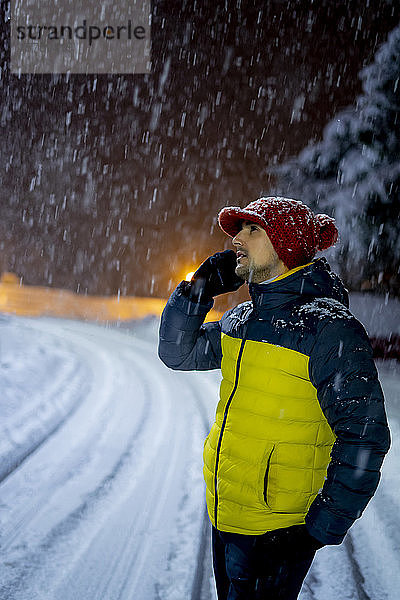 Mann am Telefon bei Schneefall in der Nacht