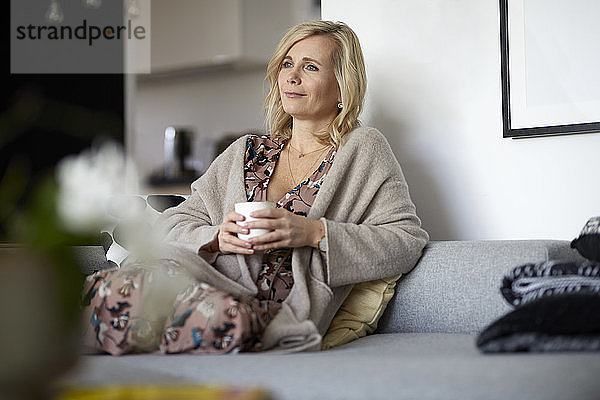 Blonde Frau entspannt zu Hause auf dem Sofa sitzend