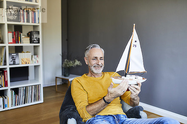 Lächelnder reifer Mann zu Hause mit Modell-Segelboot