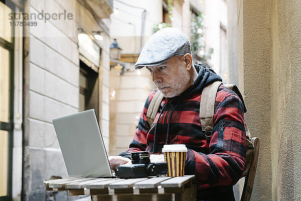 Porträt eines älteren Mannes  der mit einem Laptop in einem Straßencafé sitzt  Barcelona  Spanien