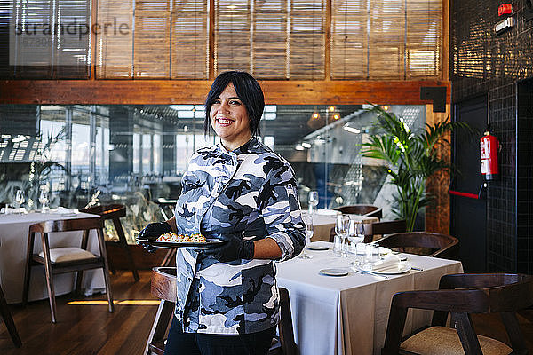 Porträt einer lächelnden Frau  die im Restaurant ein Gericht serviert