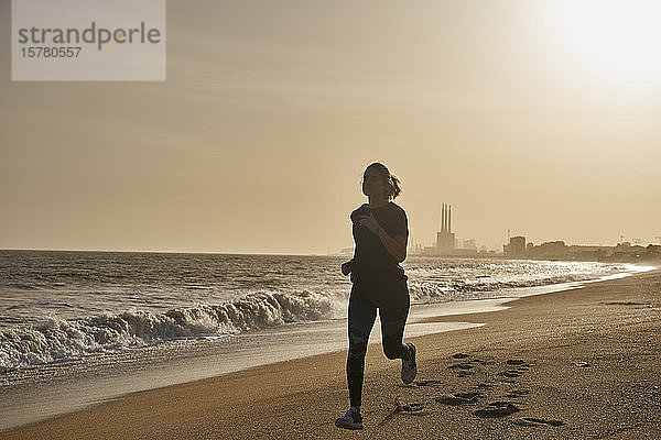 Junge Frau rennt bei Sonnenuntergang am Strand