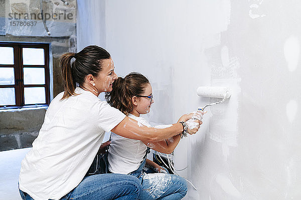 Mutter und Tochter streichen gemeinsam eine Wand ihres neuen Hauses
