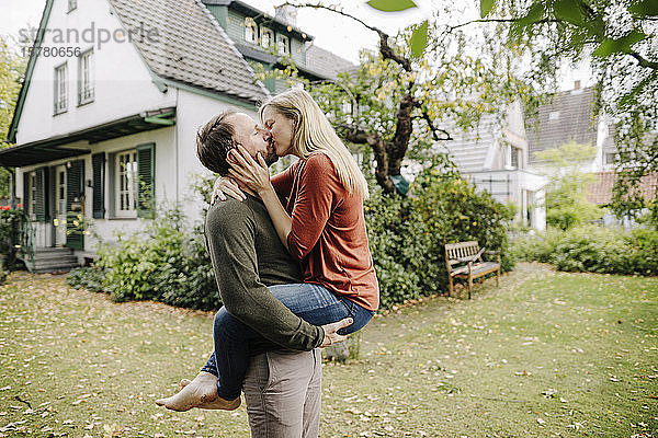 Glückliches Paar küsst sich im Garten  vor ihrem Traumhaus