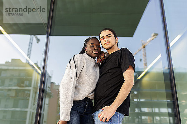 Porträt eines selbstbewussten jungen Paares an einer Glasfront stehend