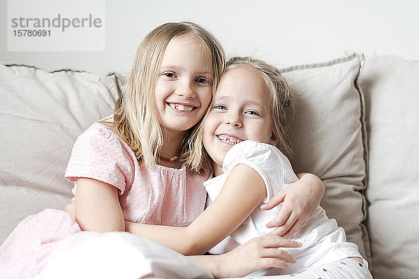 Porträt von zwei kleinen Mädchen  die sich auf der Couch umarmen