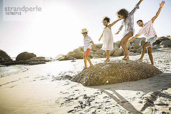 Glückliche Familie balanciert auf einem Felsen am Strand