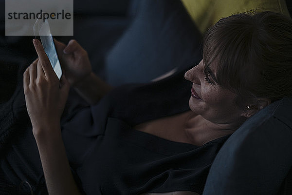 Lächelnde Frau benutzt Mobiltelefon auf der Couch