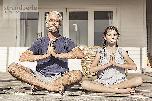 Vater und Tochter sitzen bei Sonnenschein auf der Terrasse und machen Yoga