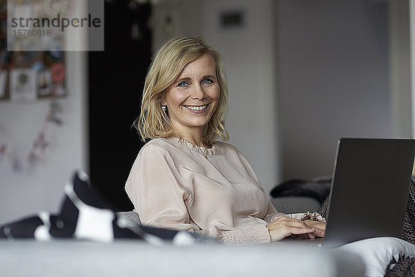 Porträt einer lächelnden blonden Frau  die zu Hause einen Laptop benutzt