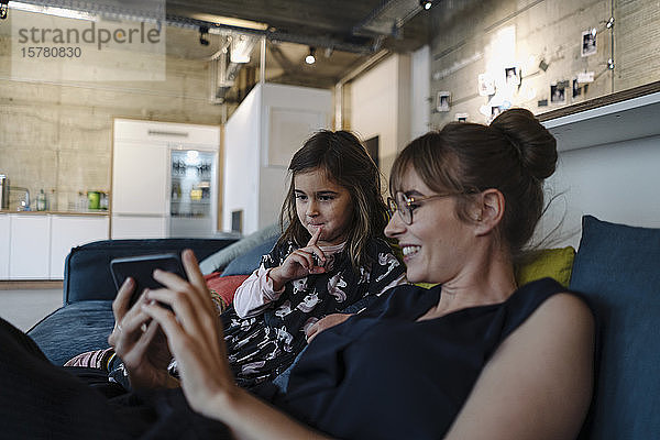 Frau und Mädchen sitzen im Büro auf der Couch und benutzen ein Smartphone