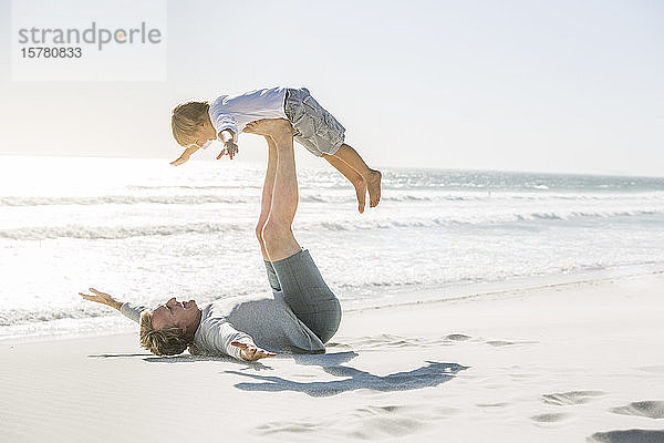 Vater amüsiert sich mit seinem Sohn am Strand und tut so  als würde er fliegen
