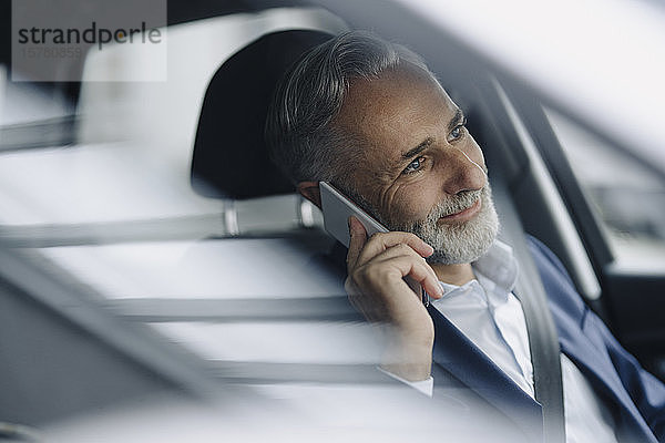 Porträt eines lächelnden reifen Geschäftsmannes am Telefon in seinem Auto