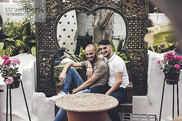 Glückliches schwules Paar sitzt zusammen auf einer Bank auf einer Terrasse