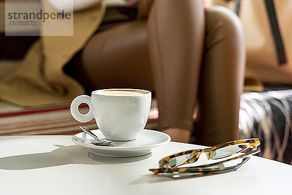 Gläser und Kaffeetasse auf Tisch in einem Café mit Frau im Hintergrund