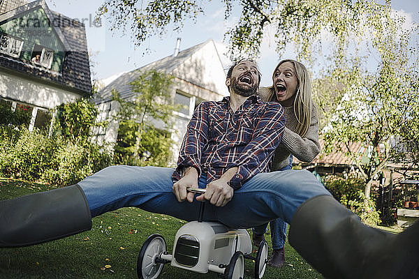 Lachendes Paar  das vorgibt  im Garten ein Spielzeugauto zu fahren