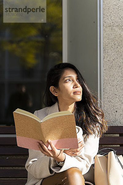 Junge Frau mit Buch auf einer Bank  die zur Seite schaut