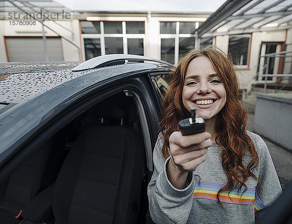 Porträt einer glücklichen rothaarigen Frau neben einem Auto mit Schlüssel