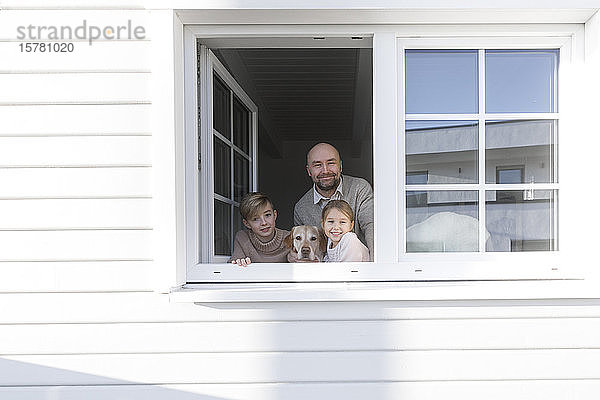 Porträt eines glücklichen Vaters und seiner beiden Kinder  die aus dem Fenster schauen