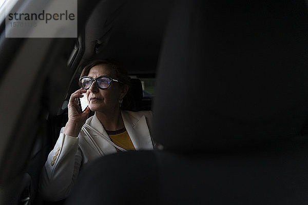 Ältere Geschäftsfrau  die in einem Taxi sitzt und ein Smartphone benutzt