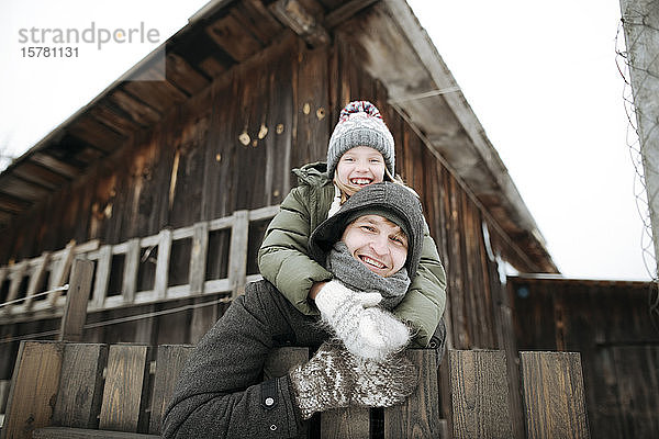 Porträt eines glücklichen Vaters  der seine Tochter im Winter huckepack nach draussen trägt