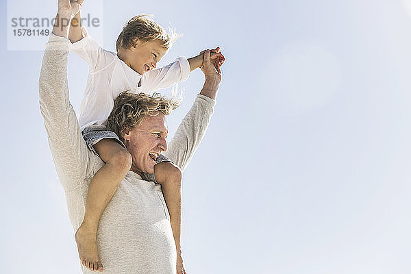 Vater amüsiert sich mit seinem Sohn am Strand und trägt ihn huckepack