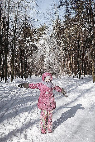 Kleines Mädchen wirft Schnee im Winterwald
